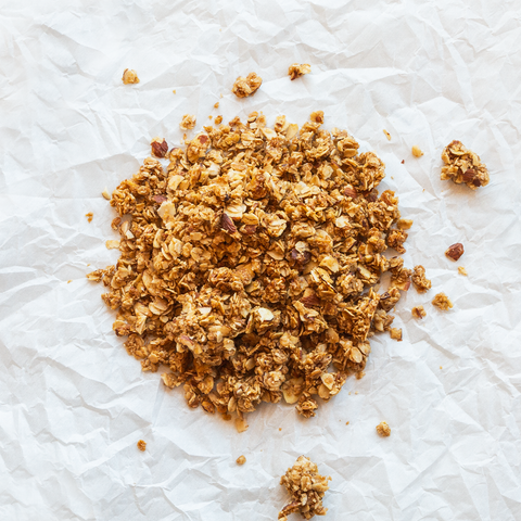 A pile of loose granola which consists of oats, almonds, and more on the background of a crumpled piece of white paper.